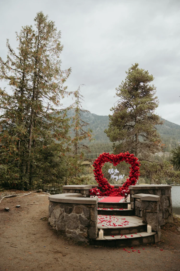 Mountain outdoor proposal with red floral arch in Whistler