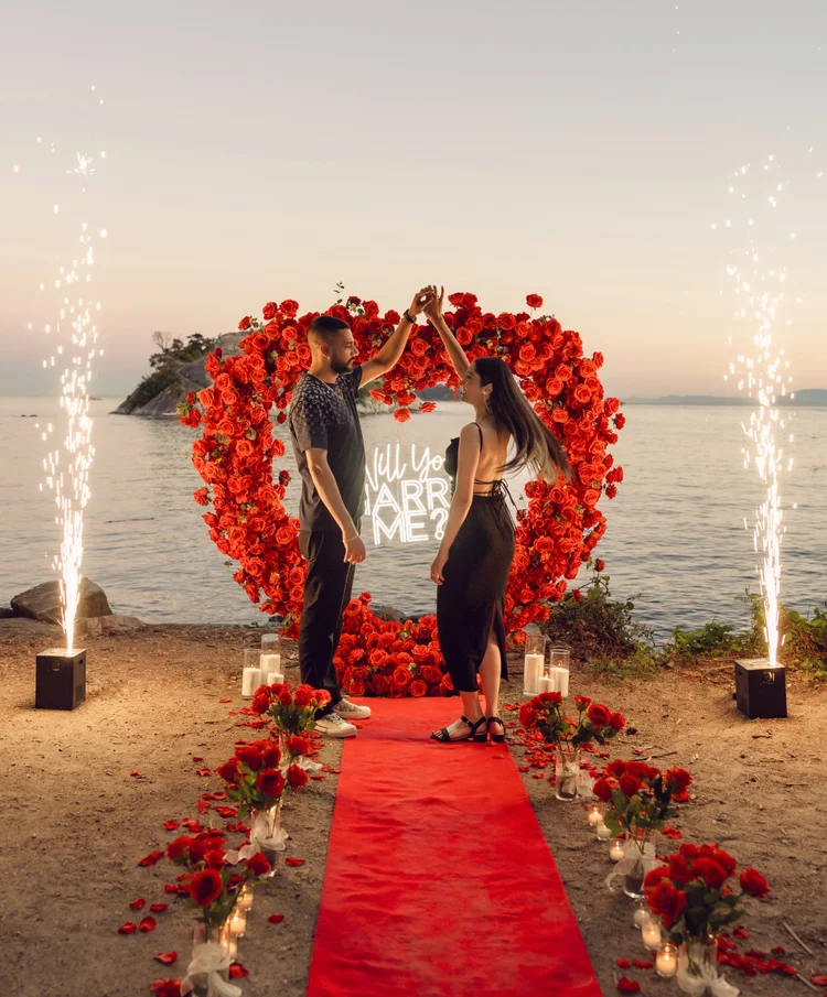 Sunset beach proposal with red floral arch and sparklers